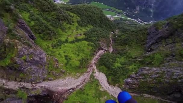 Fallschirmspringer beim Fallschirmspringen zwischen Bergen, die von Grün und Schnee bedeckt sind. Extremsport — Stockvideo