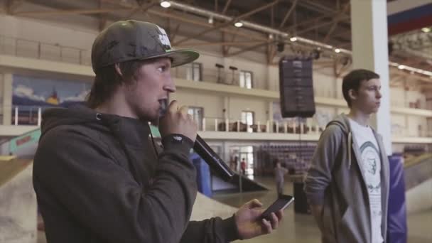 KRASNOYARSK, RUSIA - 15 DE MARZO DE 2014: Un joven con gorra habla en micrófono con teléfono en las manos en el skatepark. Desafío. Competencia — Vídeo de stock