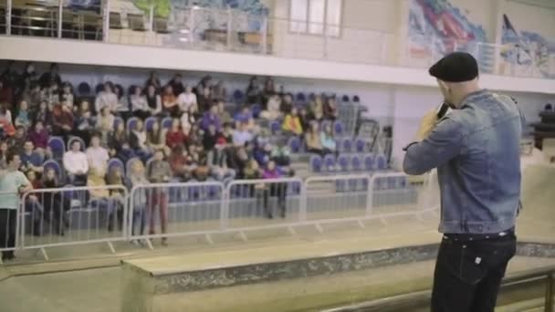 KRASNOYARSK, RUSIA - 15 DE MARZO DE 2014: La parte trasera del hombre con sombrero habla en micrófono con la gente en el parque de skate. Público. Competencia. Hostia — Vídeos de Stock