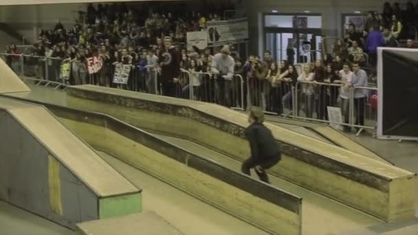 KRASNOYARSK, RUSIA - 15 DE MARZO DE 2014: Rodillo de patinador sobre valla con pies cruzados. Un trampolín. Público. Multitud. Competencia en skatepark — Vídeo de stock