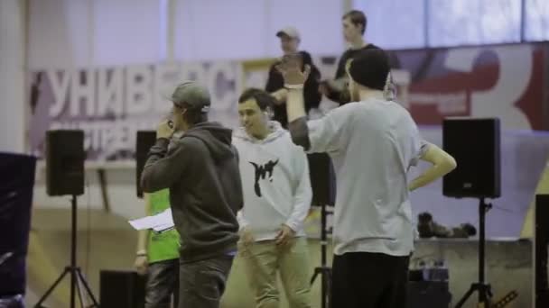 KRASNOYARSK, RUSIA - 15 DE MARZO DE 2014: Joven anfitrión en gorra con micrófono en el escenario. Patinadores. Camarógrafo. Competencia en skatepark — Vídeo de stock