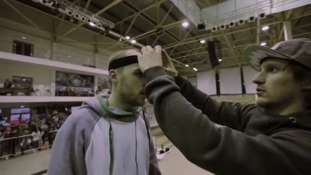 KRASNOYARSK, RUSIA - 15 DE MARZO DE 2014: El hombre con gorra puso una cámara profesional en la cabeza del patinador. Sonríe en cámara. Competencia en skatepark . — Vídeos de Stock