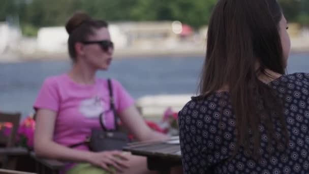 As meninas jovens sentam-se no terraço do restaurante à beira-mar. A falar. Amigos. Quadro — Vídeo de Stock