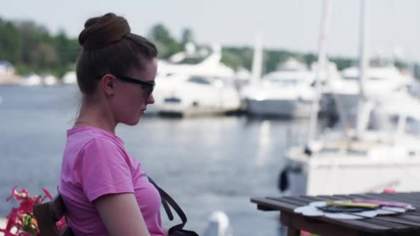 Ung flicka i solglasögon sitter på terrassen på restaurang vid havet. Vila. — Stockvideo