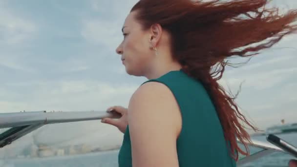 Rote Haare junge Mädchen in türkisfarbenem Kleid fahren Motorboot. Sommerabend. Wind. — Stockvideo