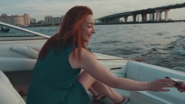 モーター ボートで赤い髪の少女。スマート フォンを取る。夏の夜します。エンターテイメント — ストック動画