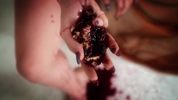 Female hand squeezes chocolate cake with berries. Juice flows between fingers — Stock Video