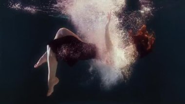 Mayolu ve siyah etekli bir kadın suda yüzüyor, kollarını ve bacaklarını sallıyor.