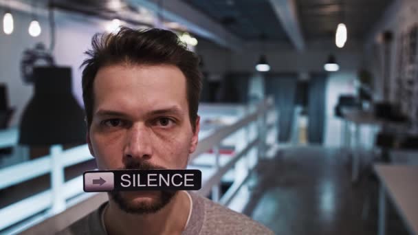 ผู้ชายมองเข้าไปในกล้องและถือป้ายในปากของเขาที่กล่าวว่า SILENCE — วีดีโอสต็อก