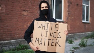 Maskeli bir adam elinde karton bir posterle ayakta duruyor.