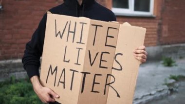 Maskeli bir adam elinde karton bir posterle ayakta duruyor.