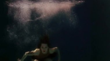 Mayolu ve siyah etekli bir kadın suda yüzüyor, kollarını ve bacaklarını sallıyor.