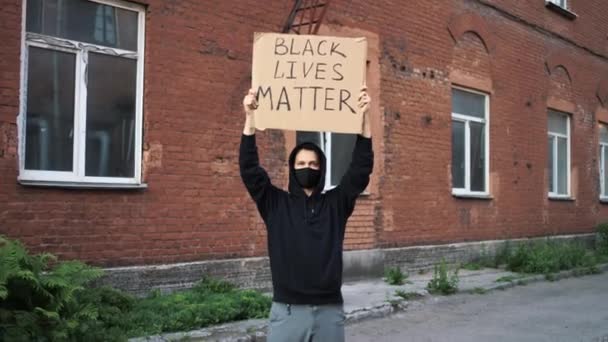 Man i mask står med kartong affisch i händerna - svart LIVES MATTER — Stockvideo