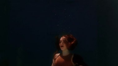 Mayolu ve siyah etekli bir kadın suda yüzüyor, kollarını ve bacaklarını sallıyor.