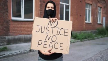 Maskeli bir adam elinde karton bir posterle ayakta duruyor.