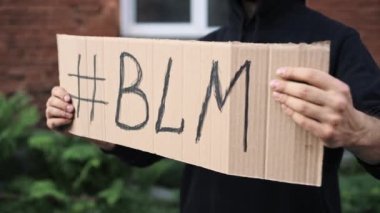 Maskeli bir adam elinde karton bir posterle ayakta duruyor.