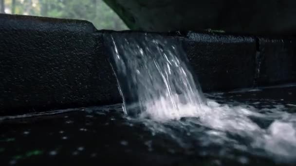 Pequena cachoeira no parque. A água derrama de uma estrutura de pedra preta — Vídeo de Stock