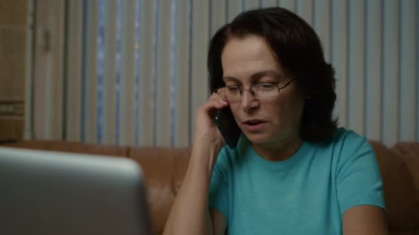 Idős nő szemüveggel és sötét hajjal izgatottan beszél okostelefonon — Stock videók