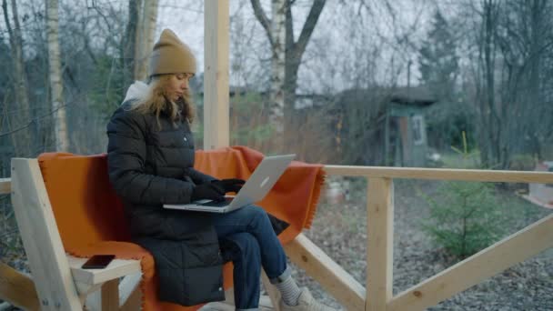ダウンジャケットの女性、冬の帽子と手袋はノートパソコンで動作します. — ストック動画