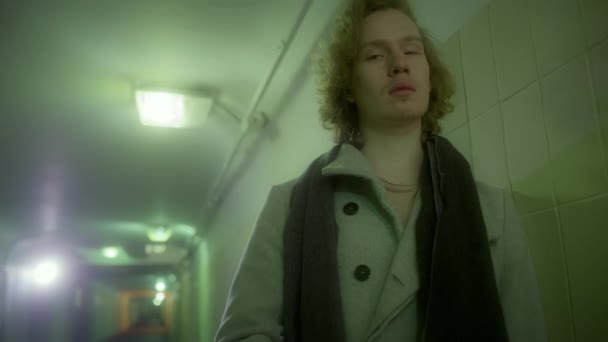 Man blond in een jas staat in de onderdoorgang en gooit een sjaal rond zijn nek. — Stockvideo