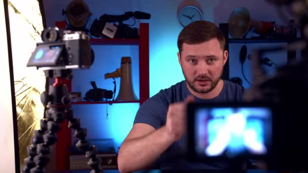 Man blogger sits at table with two cameras , red monitor and conducts video blog — Stock Video