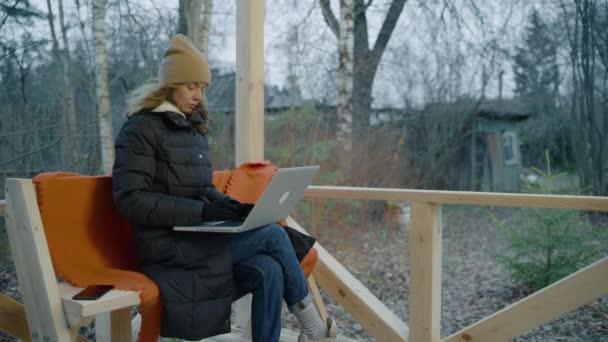 Ceketli, kışlık şapkalı ve eldivenli bir kadın dizüstü bilgisayarla çalışıyor.. — Stok video