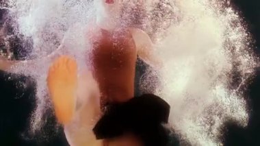 Mayolu ve siyah etekli bir kadın suda yüzüyor, kollarını ve bacaklarını sallıyor.