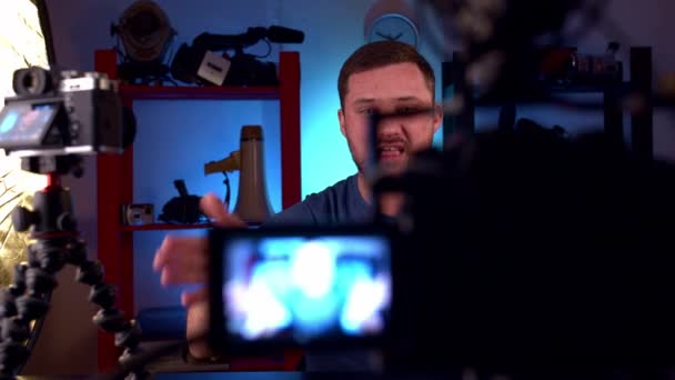 Man blogger zit aan tafel met twee camera 's, rode monitor en voert video blog — Stockvideo