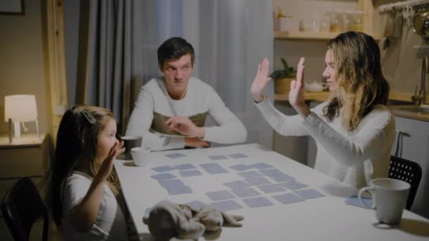 Отец семьи мама и дочь играют в настольные карточные игры за столом — стоковое видео