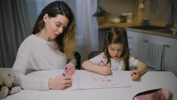 Eine Mutter und eine kleine Tochter zeichnen in der Küche mit Filzstiften Zeichnungen auf Papier — Stockvideo