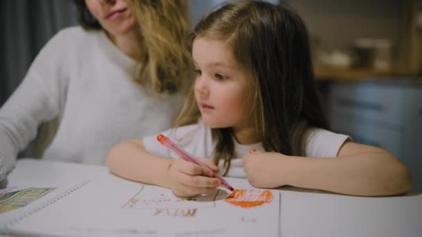 Une mère et une petite fille dessinent des dessins sur papier dans la cuisine avec des marqueurs — Video