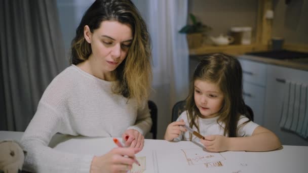 Matka a malá dcera kreslí kresby na papír v kuchyni se značkami — Stock video