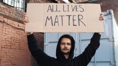 Kafkasyalı adam sokakta megafon ve tabelalarla protesto ediyor.