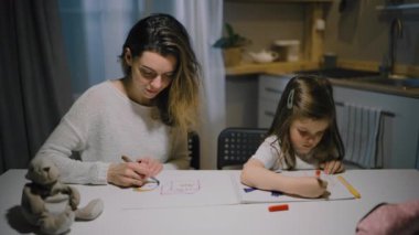Bir anne ve küçük bir kız, mutfaktaki kalemlerle kağıt üzerine çizimler yapıyorlar.