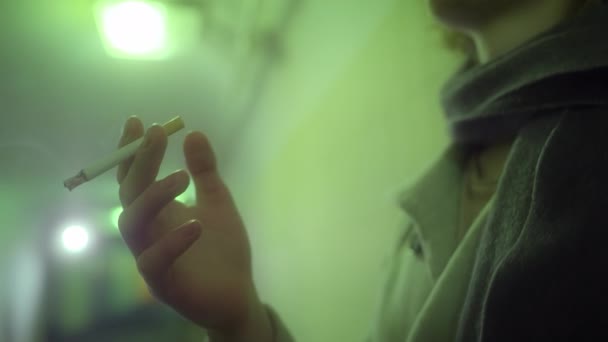 Ένας ξανθός με παλτό καπνίζει ένα τσιγάρο και κοιτάζει την κάμερα. — Αρχείο Βίντεο