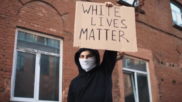 Человек в маске стоит с картонным плакатом в руках - белое имеет значение — стоковое видео