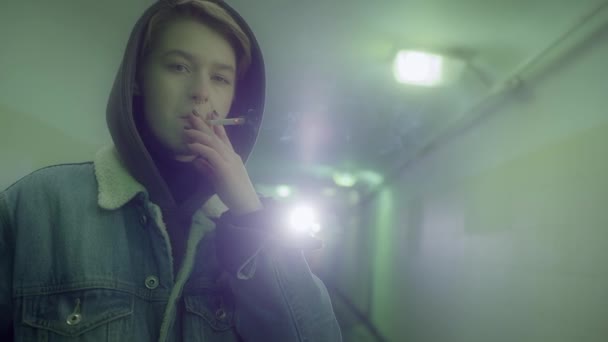 Femme avec une coupe de cheveux courte dans les stands et fume dans le passage inférieur. — Video