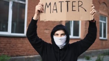 Maskeli bir adam elinde karton bir posterle ayakta duruyor.