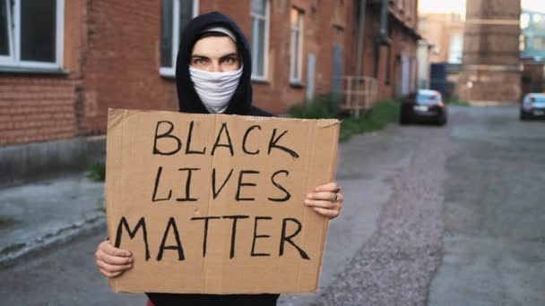 Mann i maske står med pappplakat i hender - BLACK LIVES MATTER – stockvideo