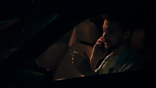 Mand sidder i bilen om natten, ryger en cigaret og taler i telefon. – Stock-video