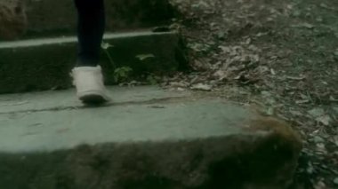 Palto giymiş küçük bir kız merdivenler boyunca koşar ve ağaçlı bir parkta çimenler