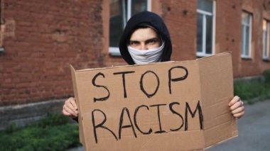 Maskeli adam elinde karton posterle ayakta duruyor. RACISM