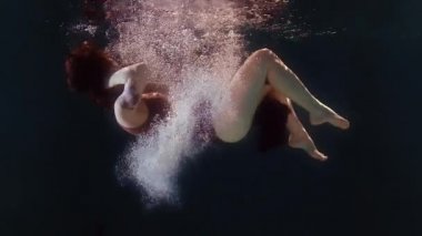 Mayolu ve siyah etekli bir kadın suda yüzüyor, kollarını ve bacaklarını sallıyor.