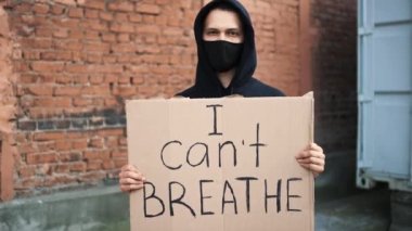 Maskeli adam elinde karton bir posterle ayakta duruyor.