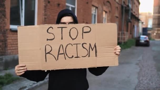 Mężczyzna w masce stoi z kartonowym plakatem w rękach - AM I NEXT AND STOP RACISM — Wideo stockowe