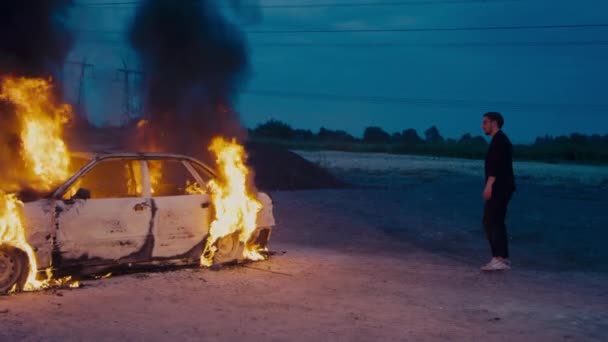 Europese man in een zakenpak loopt rond een brandende auto. — Stockvideo