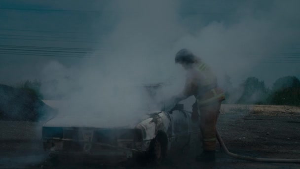 Brandweerman blust een volledig verbrande auto op straat uit. Heel veel rook.. — Stockvideo