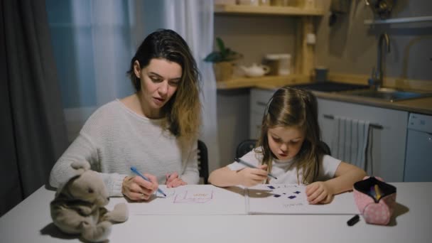 Matka i córeczka rysują rysunki na papierze w kuchni z markerami — Wideo stockowe