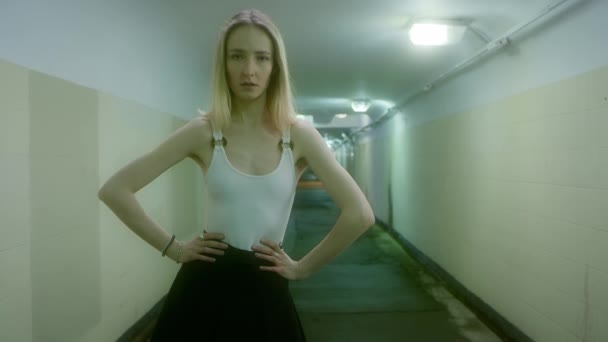 Blond kvinna i svart kjol och vit T-shirt utgör i en underjordisk passage. — Stockvideo