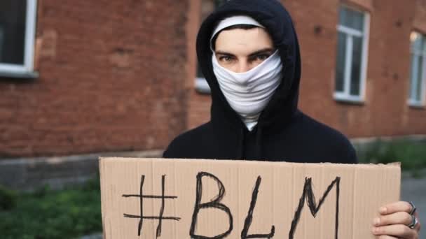 Mężczyzna w masce stoi z tekturowym plakatem w rękach - BLM — Wideo stockowe